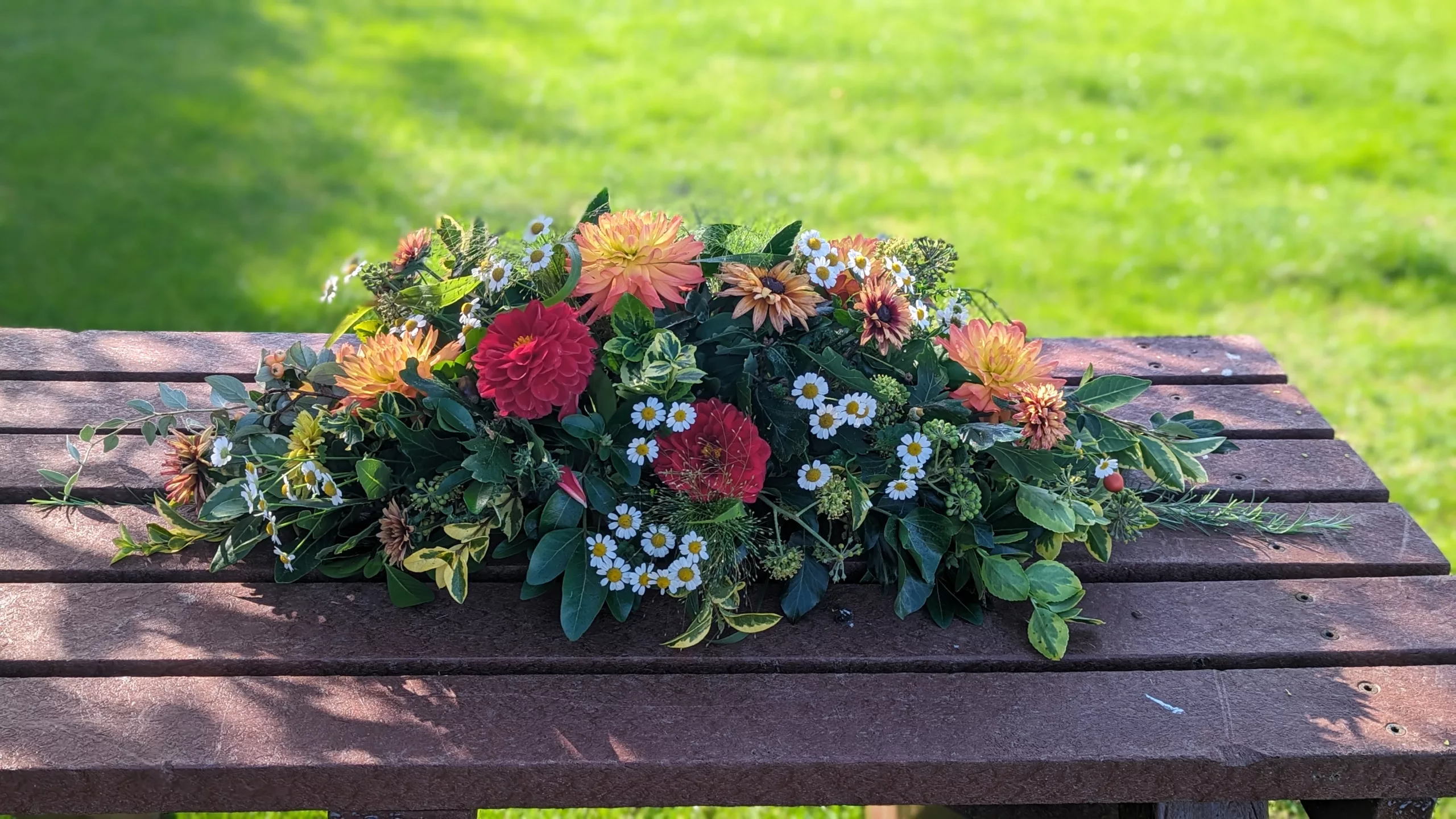 orange and red coffin spray with dahlias on a wooden table